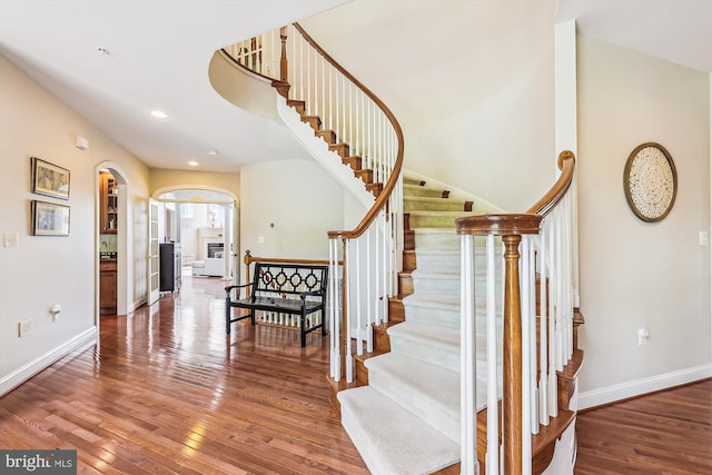 staircase with arched walkways, wood-type flooring, baseboards, and recessed lighting
