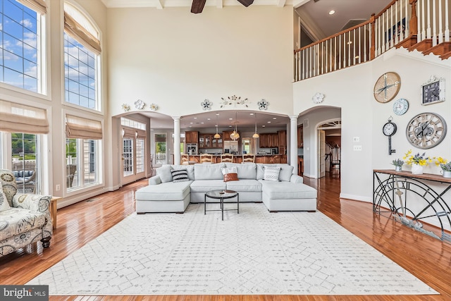 living area with decorative columns, arched walkways, a towering ceiling, healthy amount of natural light, and beamed ceiling