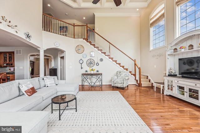 living room featuring arched walkways, a towering ceiling, stairway, wood finished floors, and ornate columns