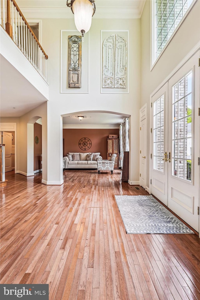 entrance foyer with a towering ceiling, arched walkways, wood-type flooring, crown molding, and baseboards