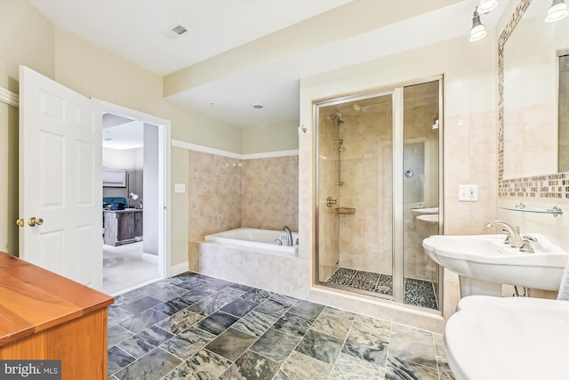 full bathroom with a stall shower, a bath, tile walls, a sink, and baseboards