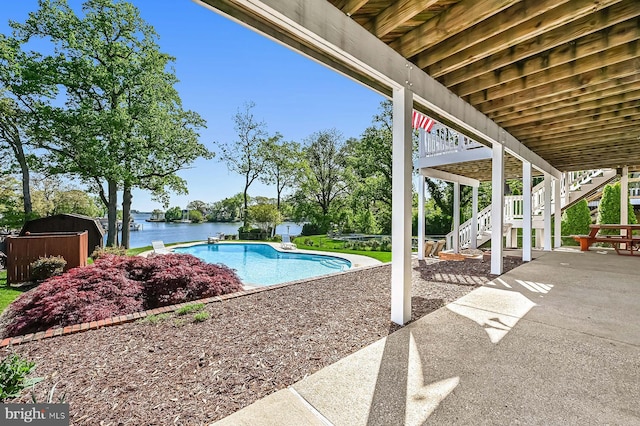 outdoor pool with a storage shed, an outbuilding, a patio area, stairway, and a water view