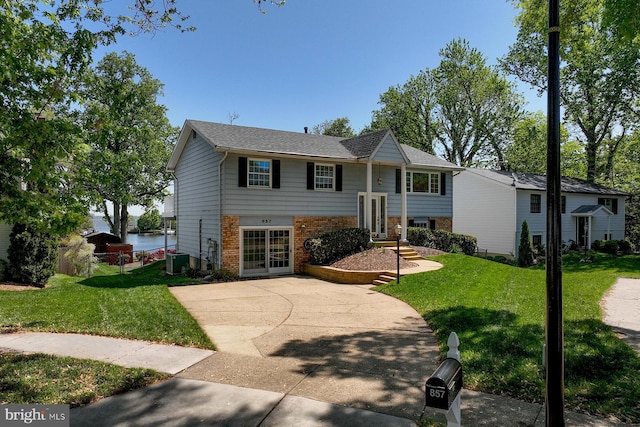 bi-level home with brick siding, central air condition unit, french doors, and a front yard