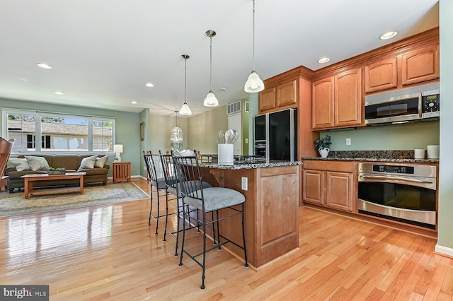 kitchen with light wood-style floors, a breakfast bar area, dark stone countertops, stainless steel appliances, and a kitchen island
