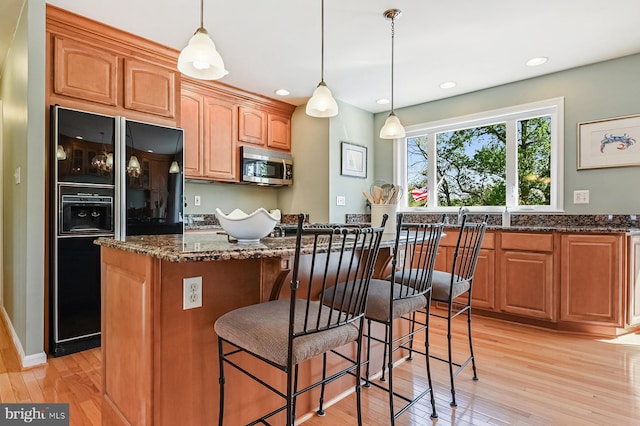 kitchen with stainless steel microwave, black fridge with ice dispenser, dark stone countertops, and light wood-style flooring