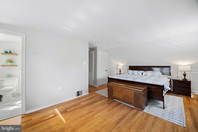 bedroom featuring visible vents, wood finished floors, baseboards, lofted ceiling, and ensuite bathroom
