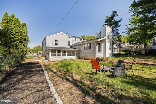 rear view of house with fence, a chimney, a sunroom, an outdoor fire pit, and a yard