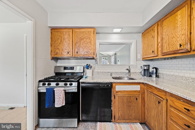 kitchen featuring brown cabinetry, stainless steel range with gas cooktop, light stone counters, a sink, and dishwasher