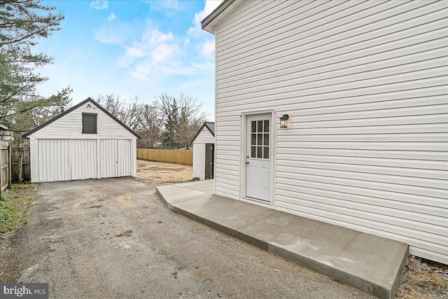 view of patio / terrace featuring an outdoor structure, aphalt driveway, and fence
