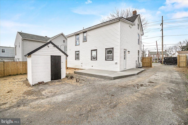back of house with a storage unit, an outdoor structure, fence, and a chimney