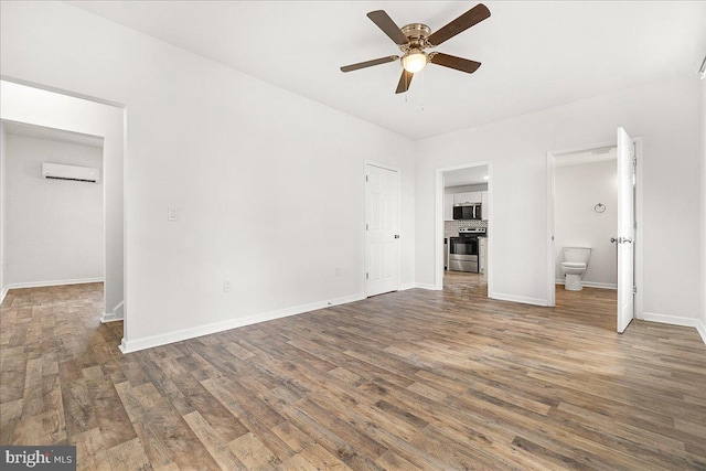 unfurnished bedroom featuring baseboards, wood finished floors, ensuite bathroom, and a wall mounted air conditioner