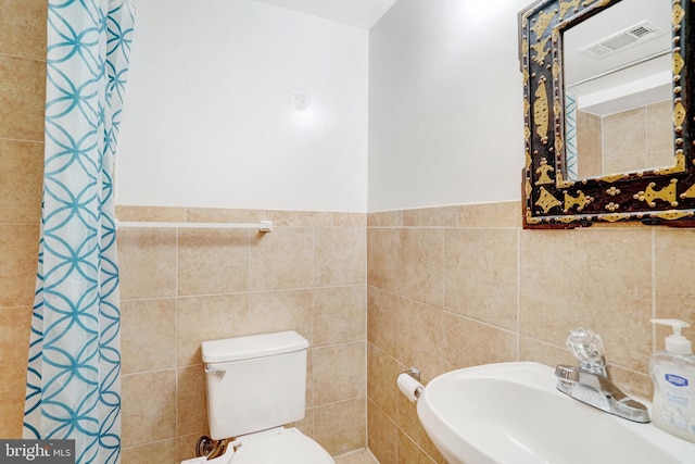 full bathroom featuring a sink, tile walls, toilet, and visible vents