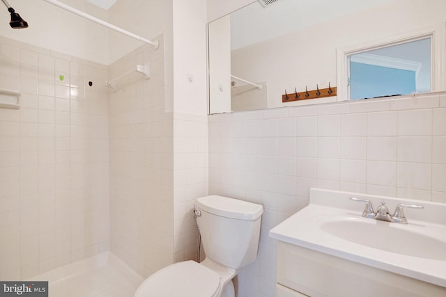 bathroom featuring visible vents, tile walls, a tile shower, vanity, and toilet
