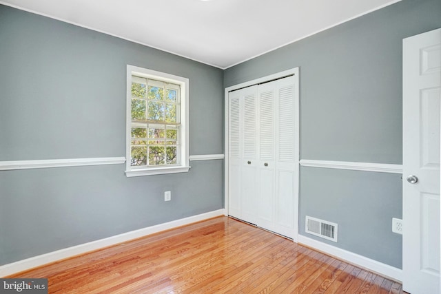 unfurnished bedroom with baseboards, a closet, wood finished floors, and visible vents
