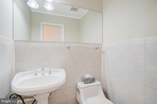half bathroom with a sink, tile walls, toilet, and visible vents