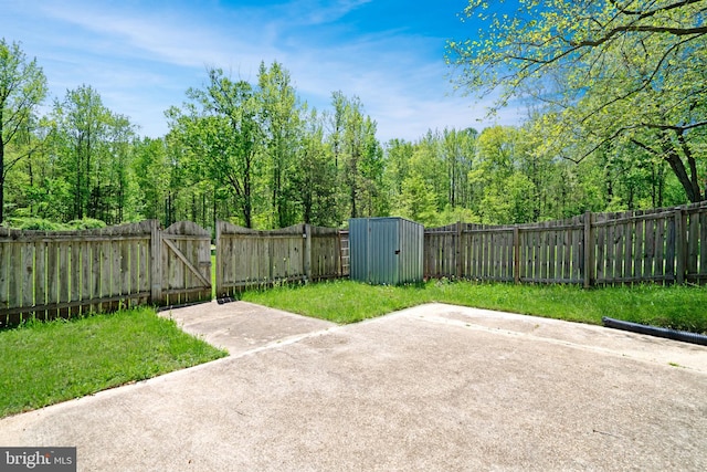 view of patio / terrace featuring an outdoor structure, a fenced backyard, a gate, a view of trees, and a storage shed