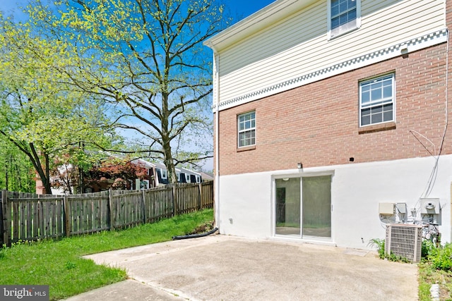 rear view of property featuring a patio area, central air condition unit, brick siding, fence, and stucco siding