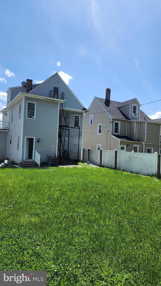 rear view of house with a yard, fence, a chimney, and cooling unit