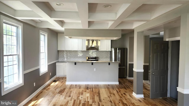 kitchen with wall chimney range hood, decorative backsplash, light wood-type flooring, white cabinets, and freestanding refrigerator