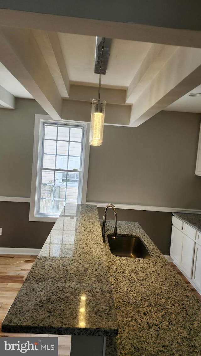 kitchen featuring dark stone counters, white cabinetry, decorative light fixtures, and a sink