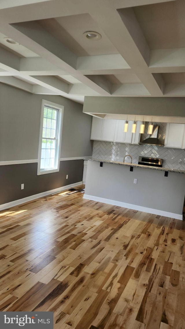 unfurnished living room with baseboards, beam ceiling, light wood-style flooring, and coffered ceiling