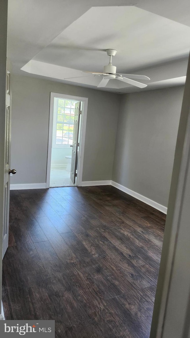 spare room featuring baseboards, ceiling fan, dark wood-style flooring, and a raised ceiling