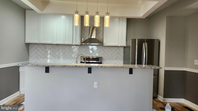 kitchen featuring decorative backsplash, range, light stone counters, a breakfast bar, and wall chimney exhaust hood