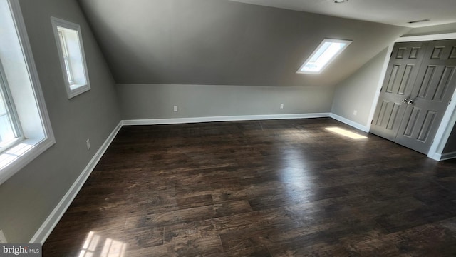 bonus room featuring baseboards, a healthy amount of sunlight, lofted ceiling with skylight, and dark wood-type flooring