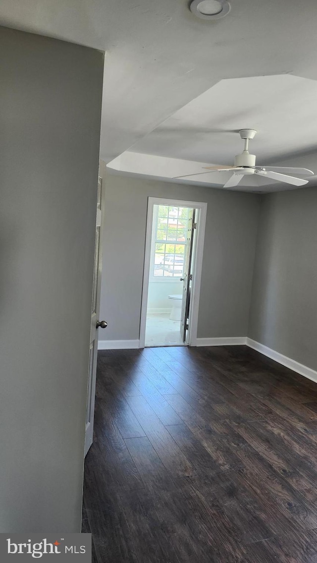 unfurnished room featuring baseboards, a ceiling fan, and dark wood-type flooring