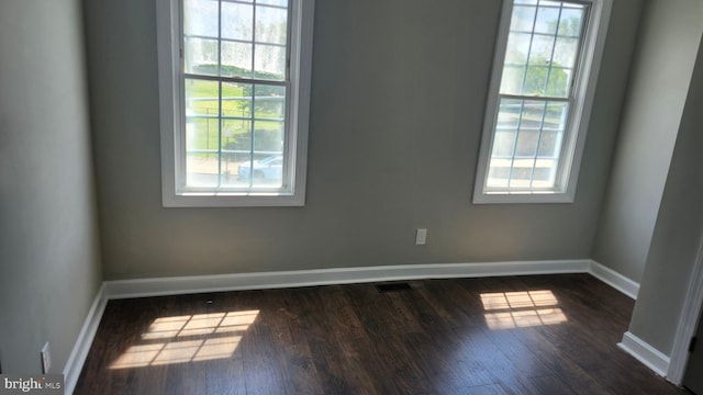 empty room with baseboards, plenty of natural light, dark wood-style flooring, and visible vents