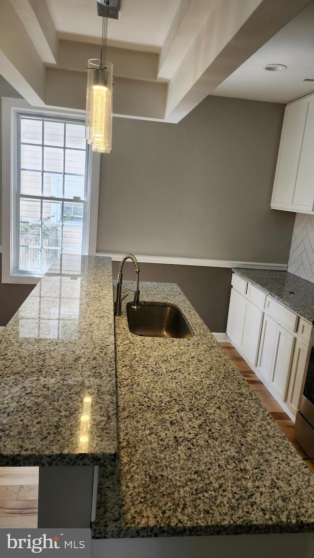 kitchen featuring a sink, hanging light fixtures, stone countertops, and white cabinets
