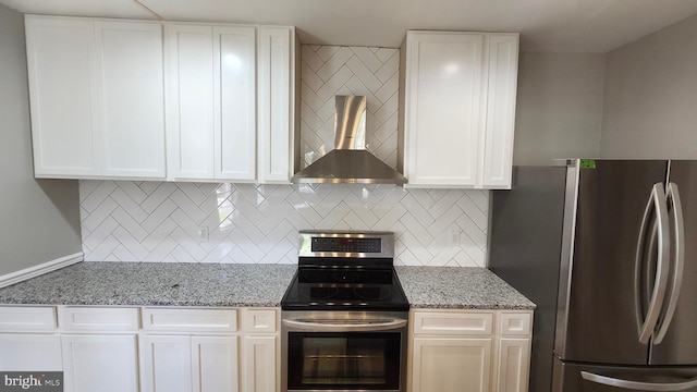 kitchen featuring wall chimney range hood, white cabinetry, tasteful backsplash, light stone counters, and stainless steel appliances