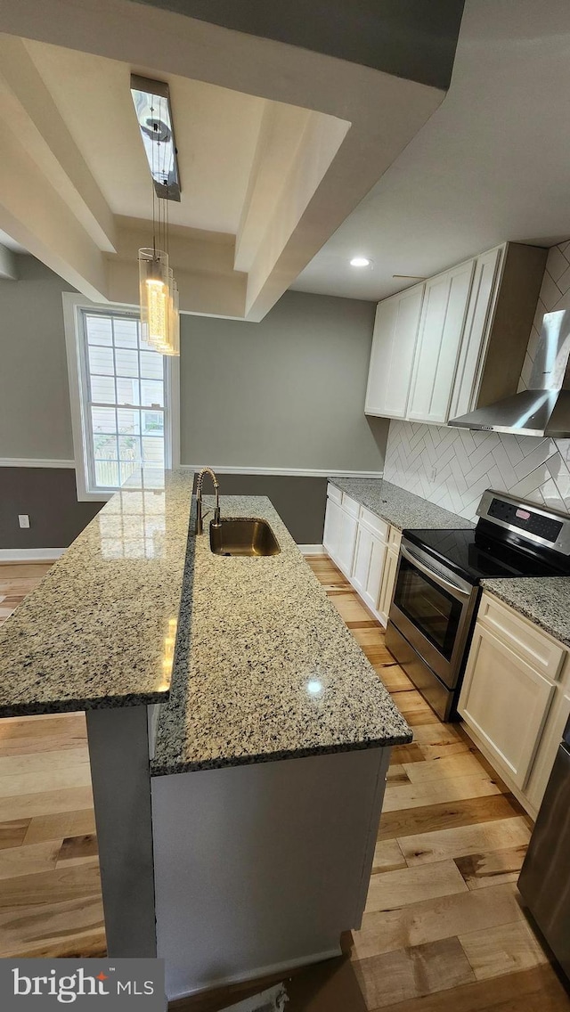kitchen with a kitchen island with sink, backsplash, stainless steel electric range, a sink, and light wood-style floors