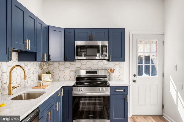 kitchen featuring a sink, blue cabinets, light wood-style flooring, appliances with stainless steel finishes, and backsplash