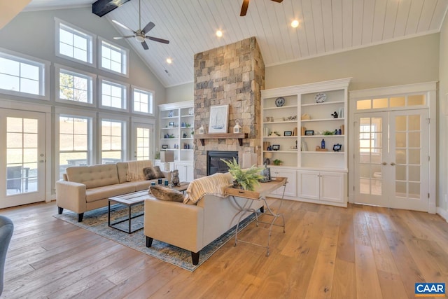 living room with french doors, light wood-style floors, ceiling fan, and a stone fireplace