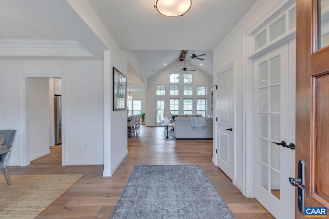 foyer entrance featuring ceiling fan, vaulted ceiling, baseboards, and light wood-type flooring