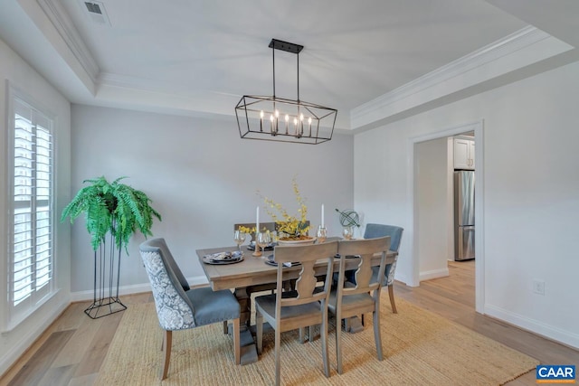 dining room featuring crown molding, light wood-style flooring, a chandelier, and a tray ceiling