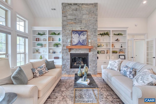 living area featuring wood ceiling, visible vents, a stone fireplace, and wood finished floors