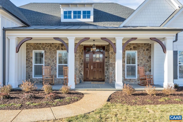 doorway to property with covered porch, roof with shingles, a standing seam roof, and stone siding