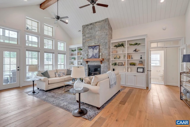 living area with a stone fireplace, a ceiling fan, high vaulted ceiling, and light wood-type flooring