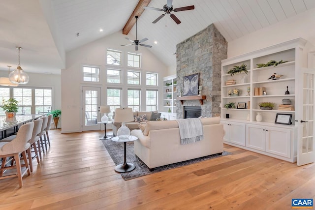 living area with beam ceiling, a stone fireplace, high vaulted ceiling, light wood-type flooring, and a ceiling fan
