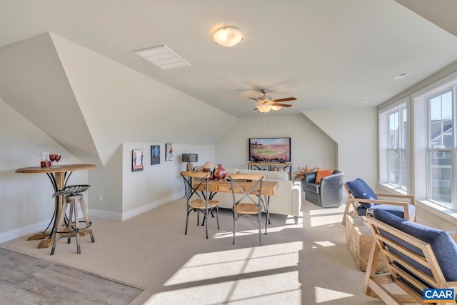 dining space with a ceiling fan, baseboards, light colored carpet, and vaulted ceiling