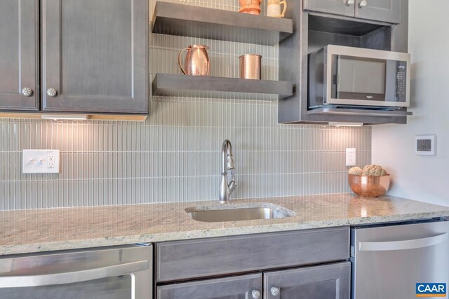 kitchen featuring open shelves, light stone counters, a sink, stainless steel appliances, and tasteful backsplash