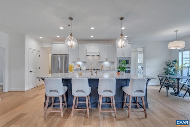 kitchen featuring stainless steel appliances, a large island, light wood finished floors, and custom range hood
