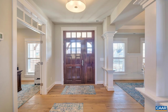 entryway featuring ornate columns, light wood-style floors, and a healthy amount of sunlight