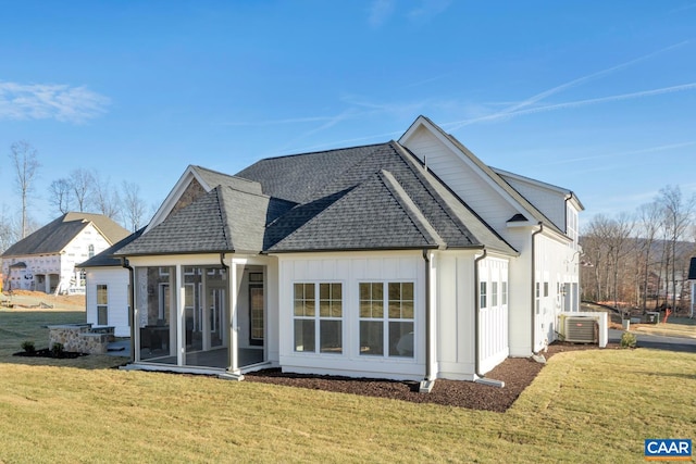 back of property with a sunroom, roof with shingles, and a lawn