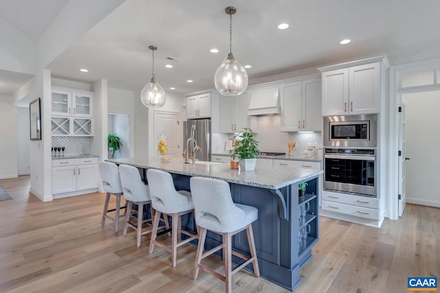 kitchen with stainless steel appliances, custom exhaust hood, white cabinetry, and tasteful backsplash