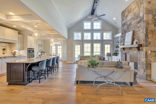 living room featuring a ceiling fan, a fireplace, light wood-type flooring, beam ceiling, and high vaulted ceiling