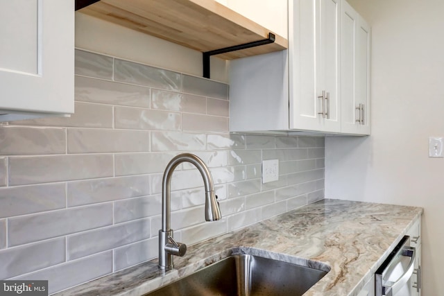 kitchen featuring tasteful backsplash, stainless steel dishwasher, a sink, light stone counters, and white cabinets