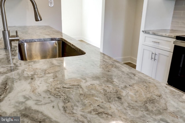 kitchen featuring white cabinets, light stone countertops, a sink, baseboards, and tasteful backsplash